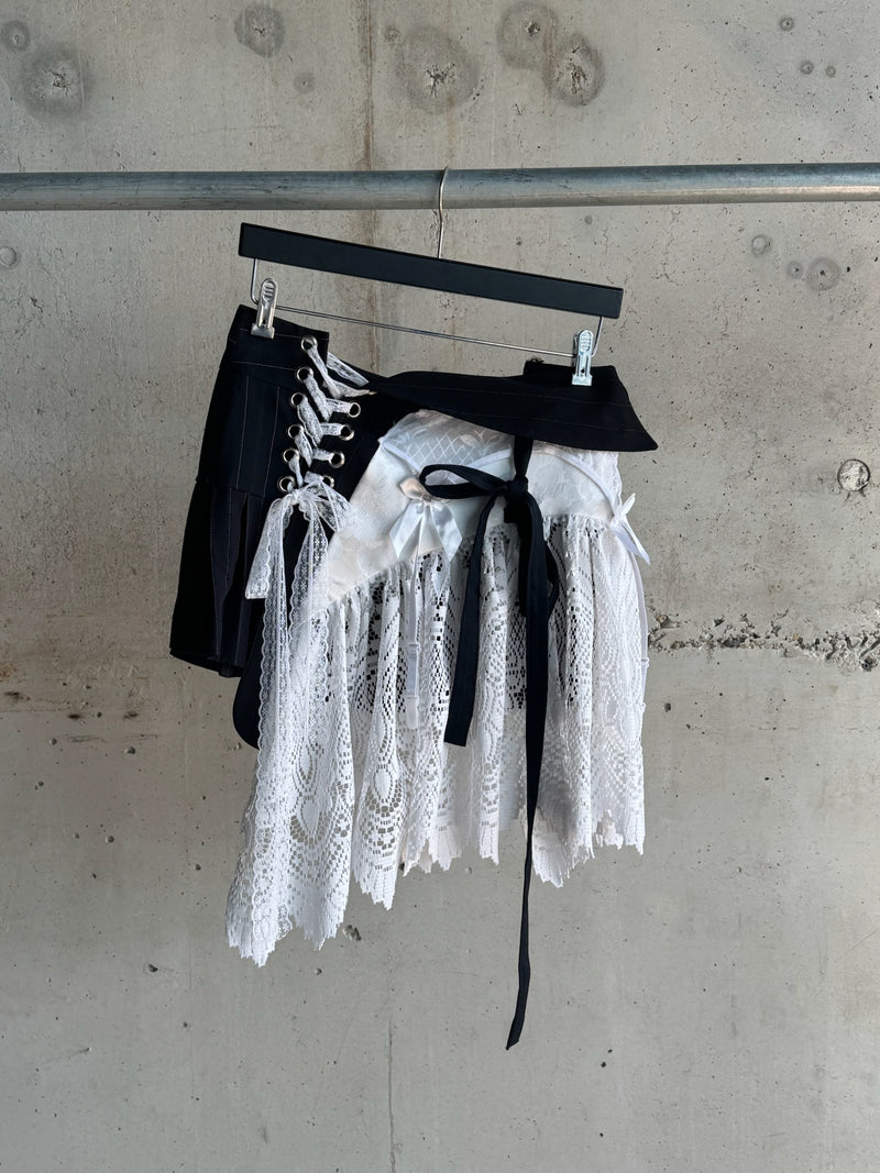 Side view of black corset skirt featuring white lace panels, lace-up grommet detailing, satin ribbon ties, and layered hem with a mix of gothic and vintage aesthetics
