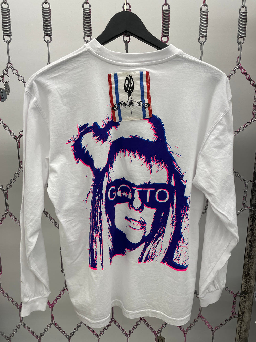 White long-sleeve shirt with graphic design of a person wearing sunglasses on a hanger against a textured wall.