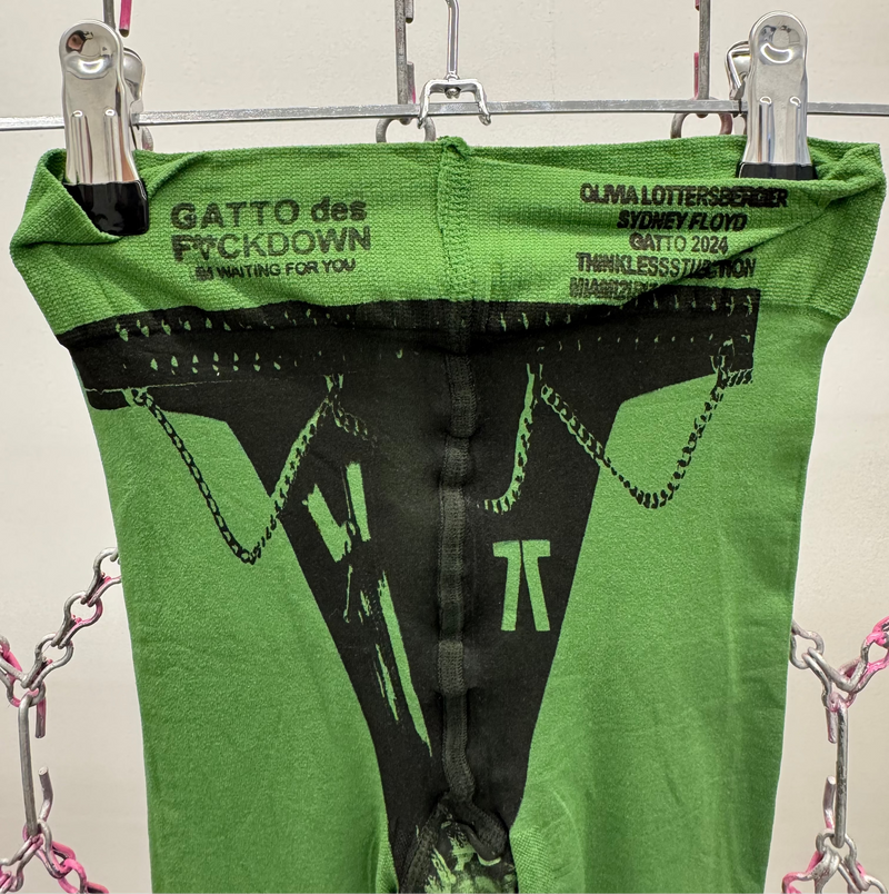 Green garment with black design and text on a hanger against a neutral background