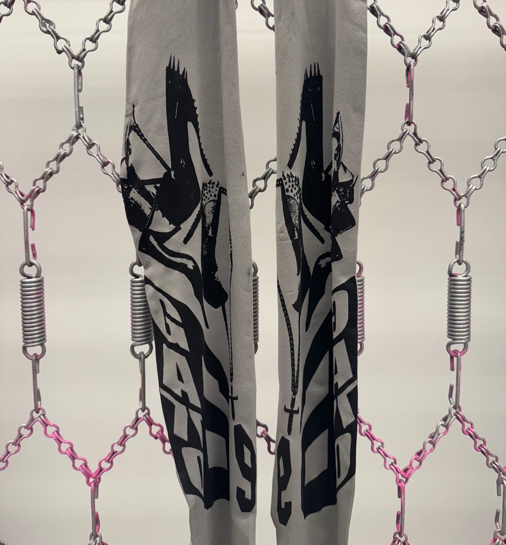 Gray pants with black graphic design and 'G-STAR' branding through a chain-link fence.