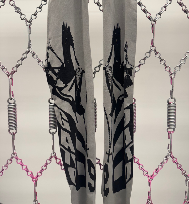 Gray pants with black graphic design and 'G-STAR' branding through a chain-link fence.