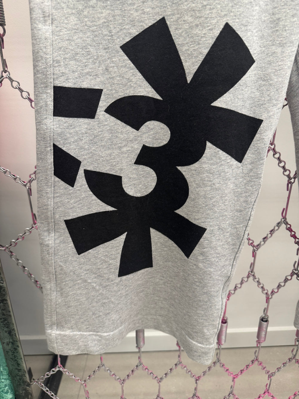 Gray sweatshirt with a black logo on a chain-link fence background