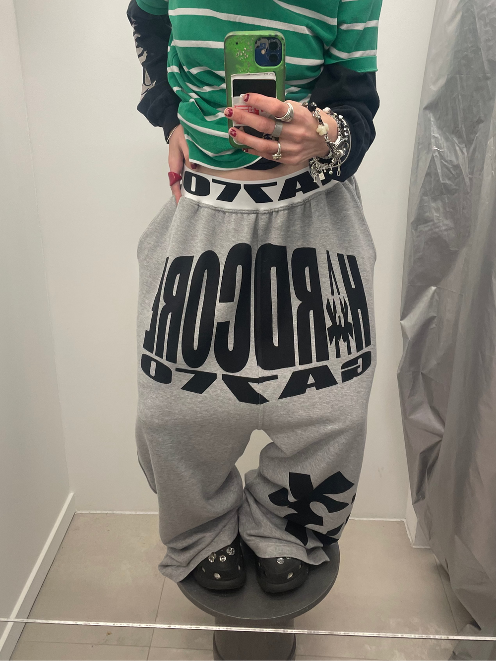 Person wearing a green and white striped shirt with gray sweatpants featuring black text, standing in a mirror.