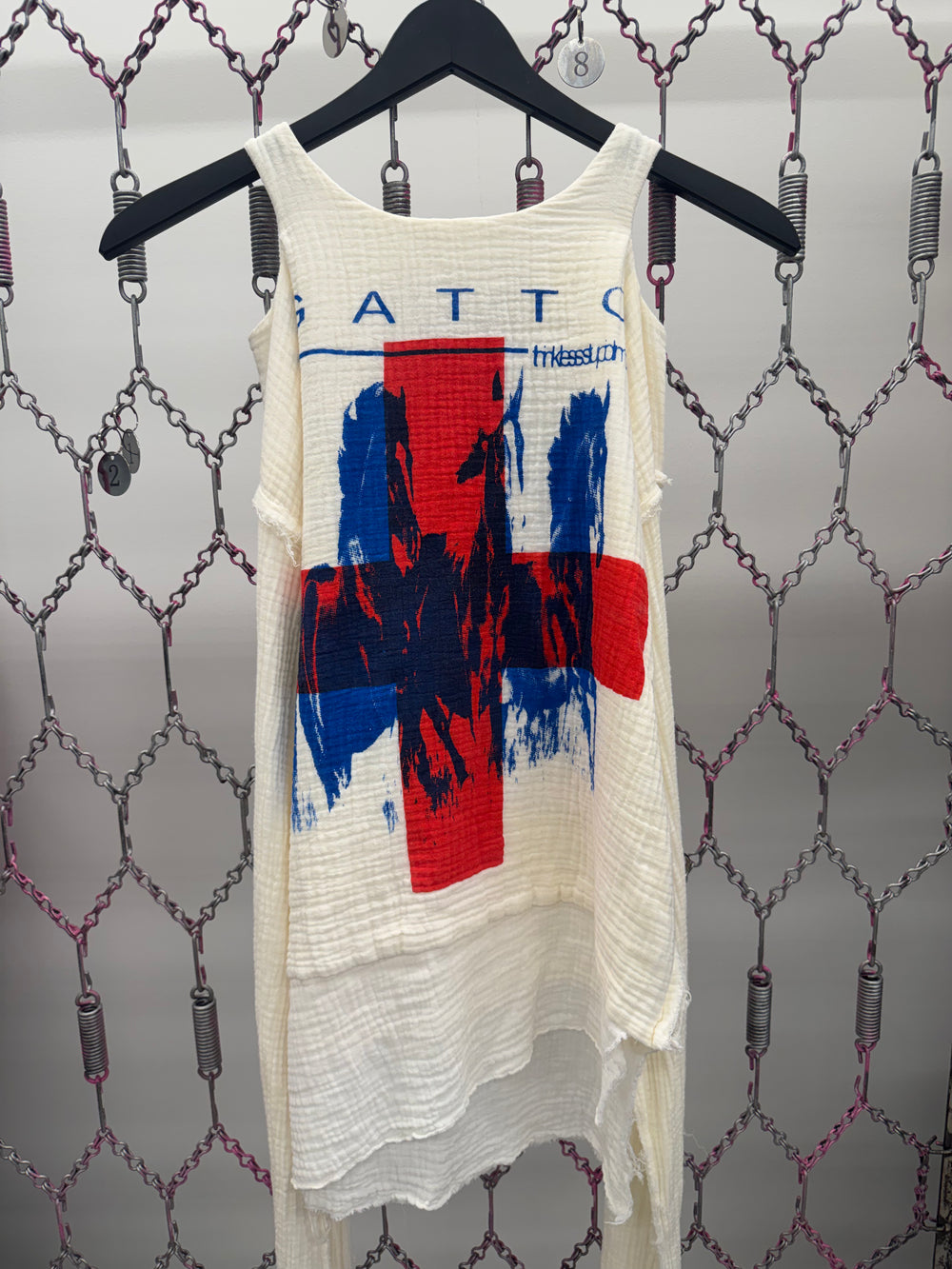 White tank top with red and blue graphic design on a hanger against a patterned wall
