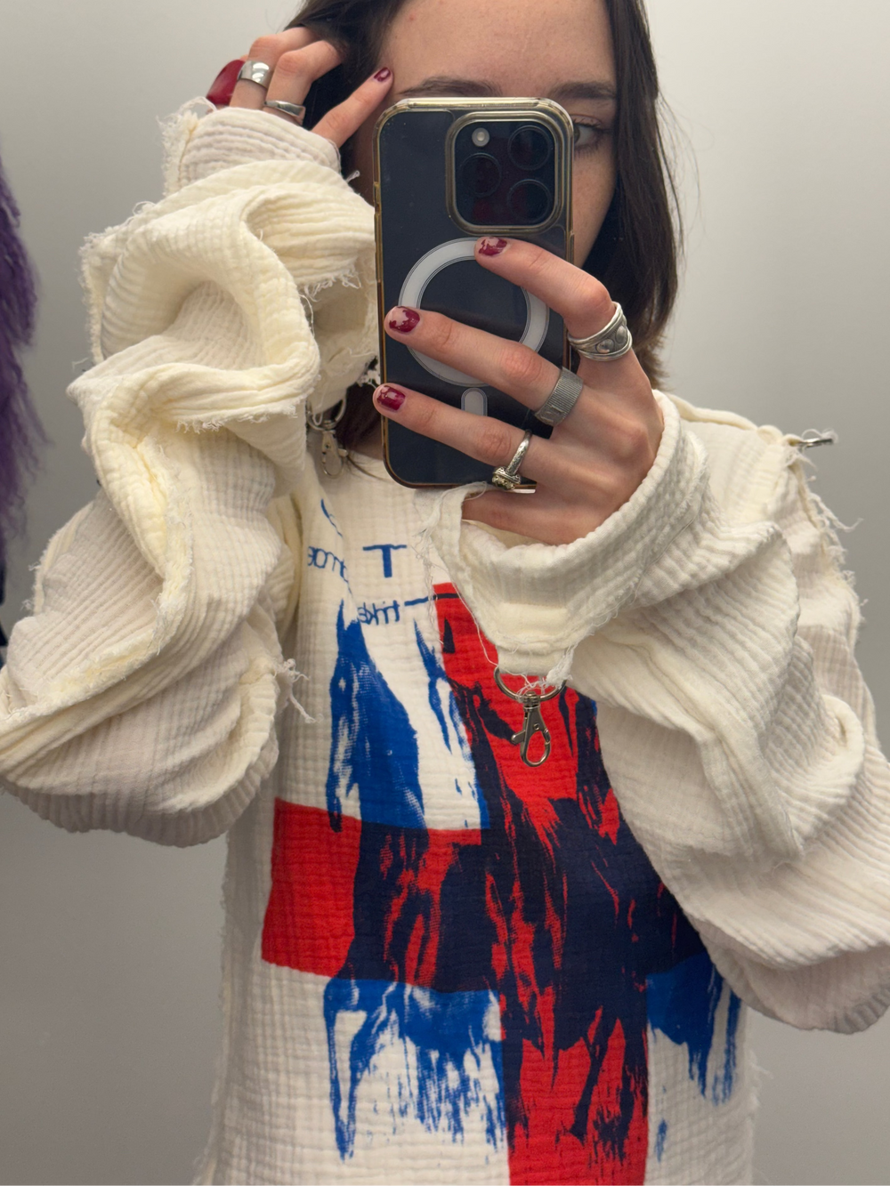 Person wearing a white sweater with a colorful abstract design, taking a mirror selfie.