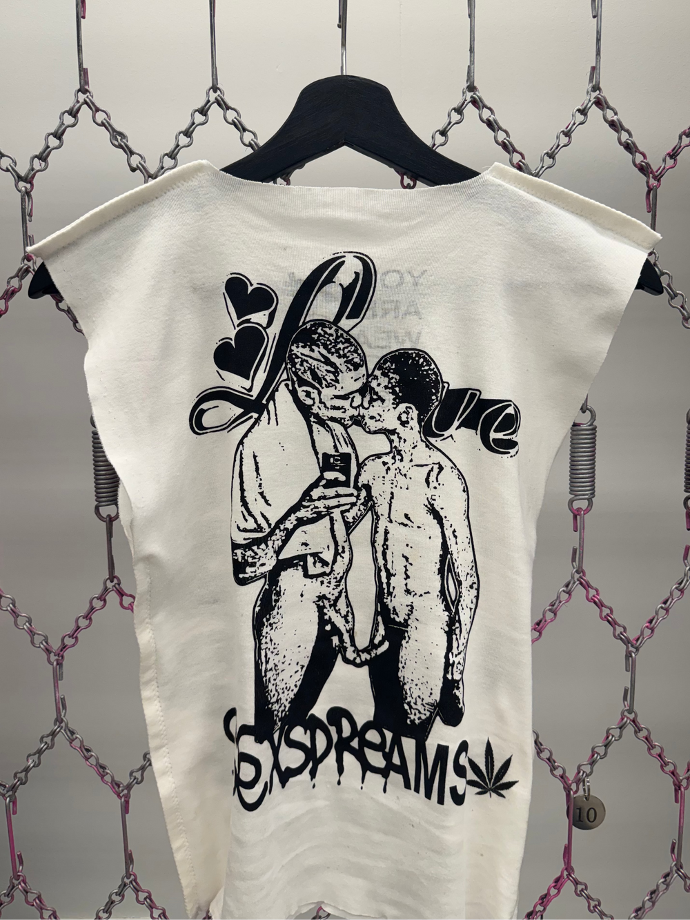 White t-shirt with black graphic design on a chain-link fence background