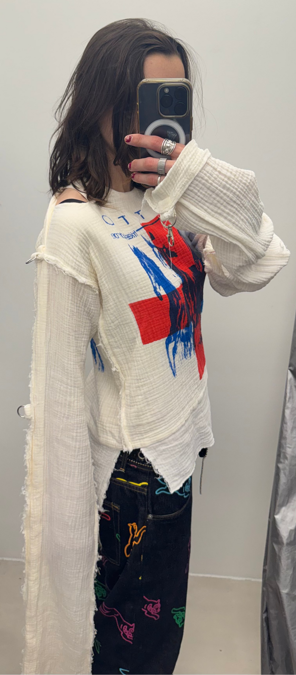 Person wearing a colorful sweater and patterned pants in a room with hanging clothes.