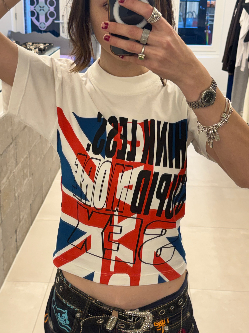 Person wearing a white t-shirt with colorful graphics and text, taking a mirror selfie.