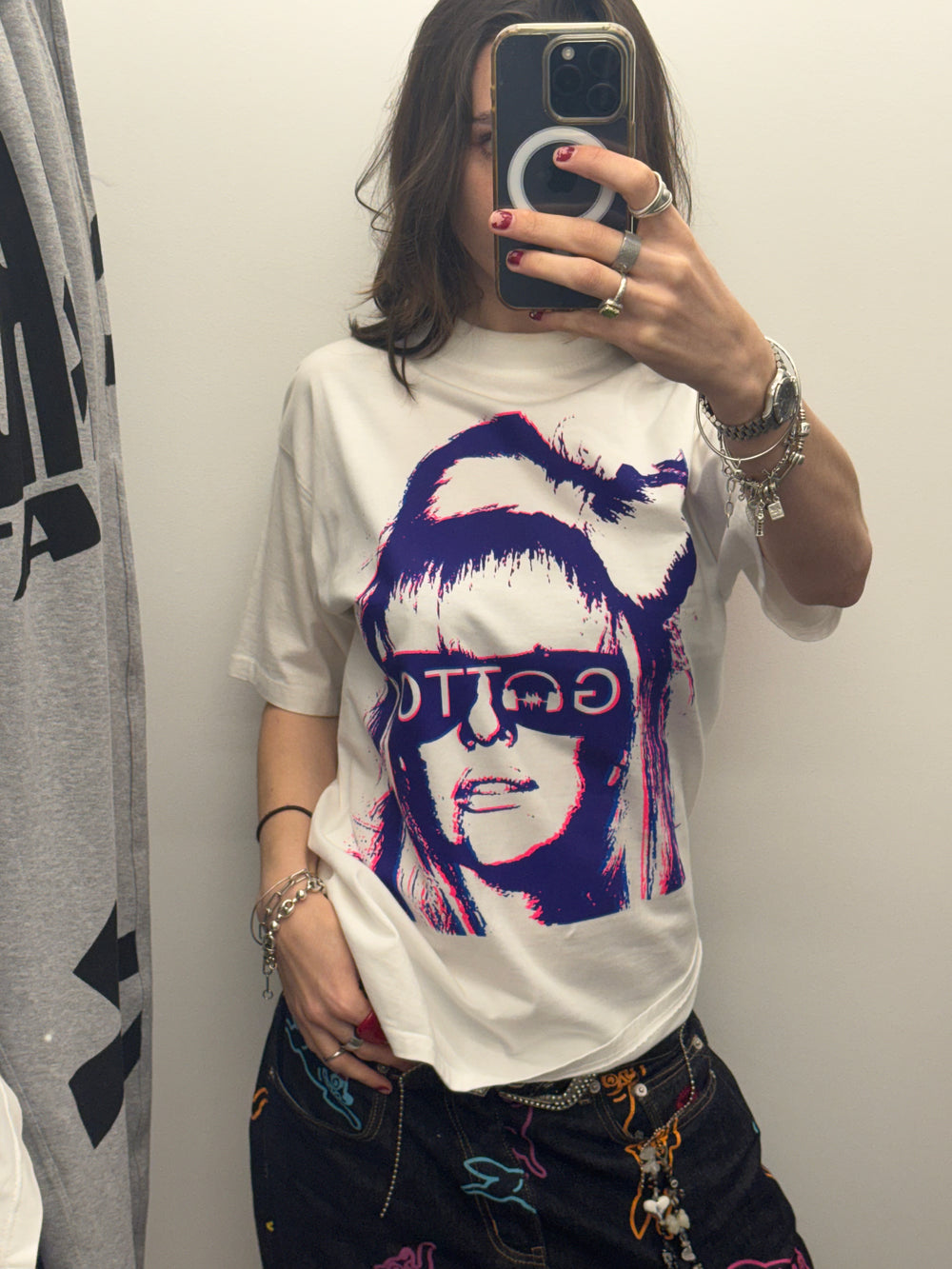 Person wearing a white t-shirt with a graphic design of a person with sunglasses and a beanie.