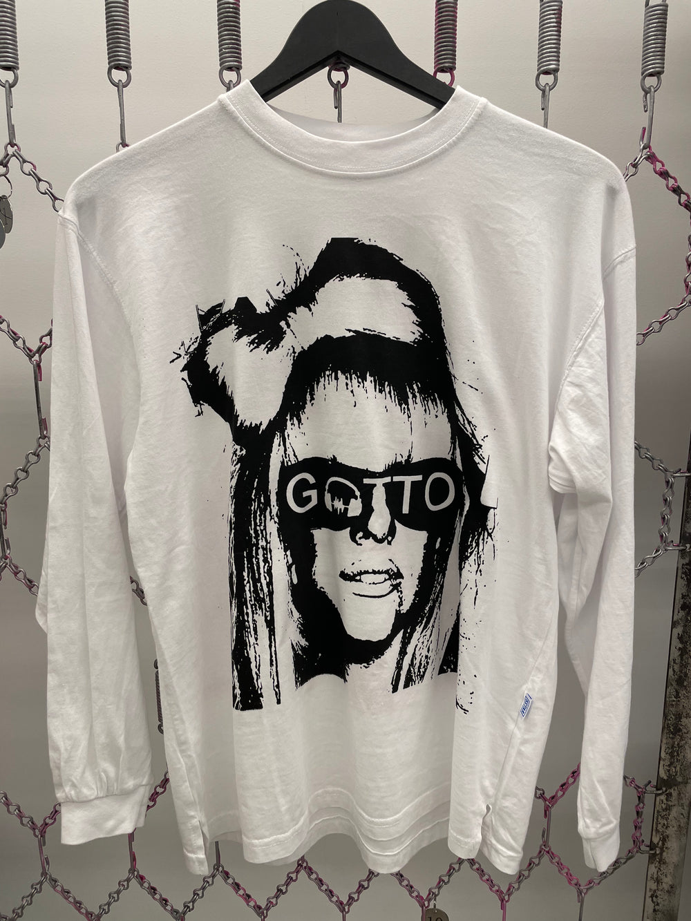 White sweatshirt with black graphic design of a face and 'GOTTO' text, hanging on a rack.