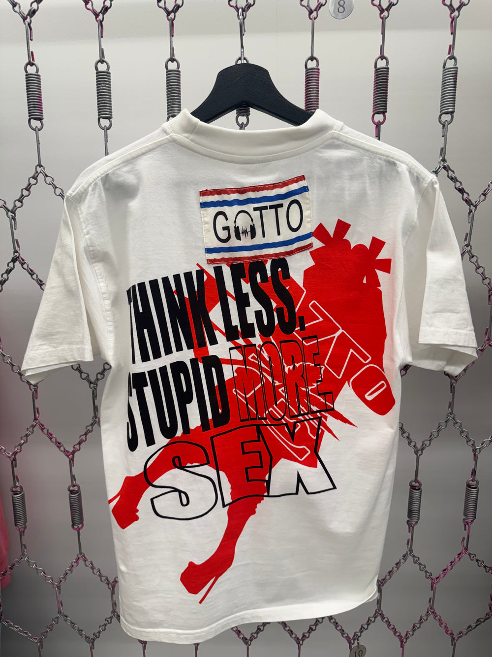 White t-shirt with graphic design and text on a chain-link fence background