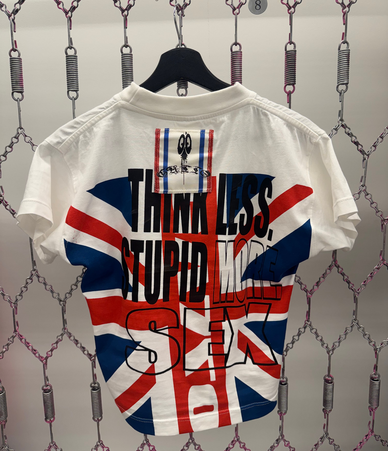 White t-shirt with British flag design and text on a hanger against a chain-link fence background