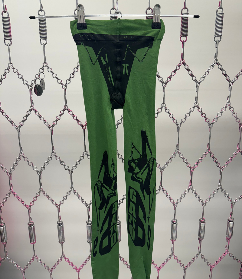 Green leggings with black designs hanging on a rack against a patterned background