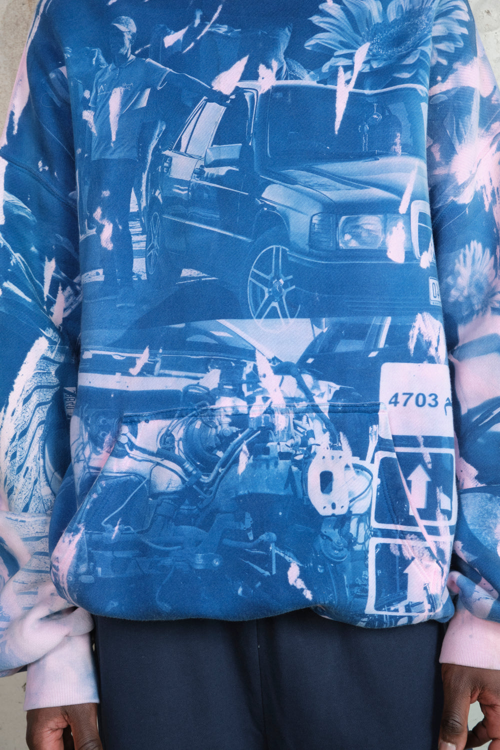 Detailed view of front graphic on oversized hoodie featuring layered collage print with car, engine, floral elements, directional sign, and street photography in blue and pink tones – printed on soft cotton fabric.