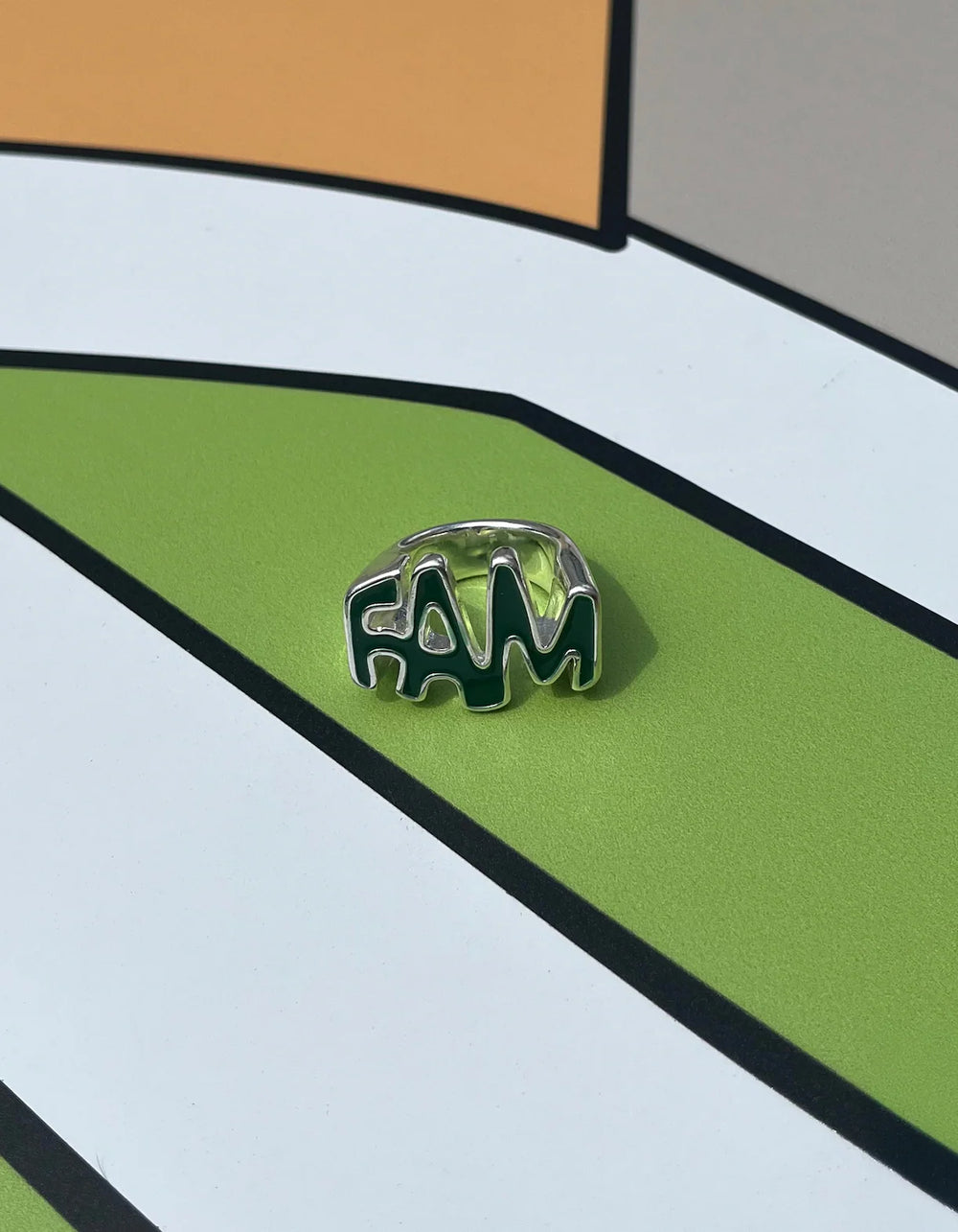 Silver ring with 'FAM' letters on a colorful geometric background