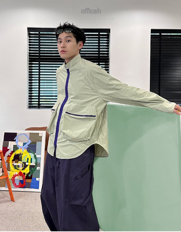 Model leaning with arm outstretched indoors
“Casual studio shot of model in sage green tech overshirt with purple zipper and patch pockets, paired with loose navy trousers – styled in minimalist interior with mint and neutral tones