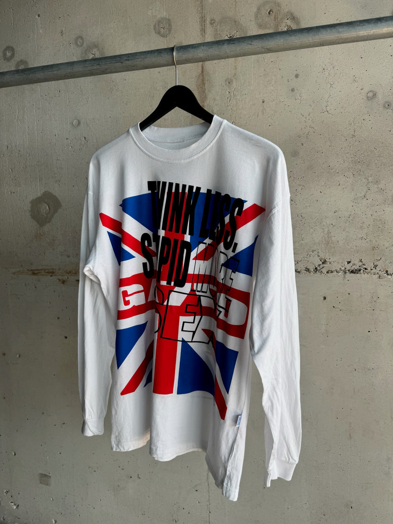 White long-sleeve T-shirt with bold black and red text “THINK LESS STUPID MORE SEX” over a vibrant Union Jack flag graphic, hanging on a black hanger against a raw concrete wall backdrop.