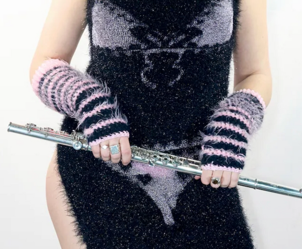 Person wearing black and pink striped mittens holding a flute against a plain background