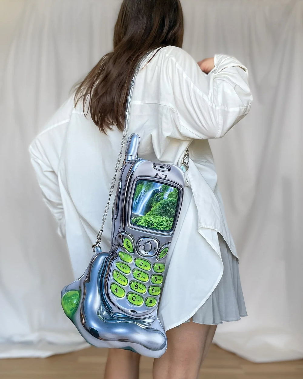 Person wearing a phone-shaped bag with a waterfall display on a plain background