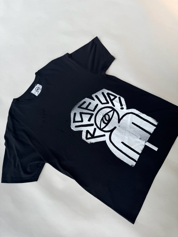 Black unisex t-shirt with bold silver graphic print featuring a stylized human figure with a single central eye and the powerful slogan ‘RISE UP!’ in hand-drawn, graffiti-style typography. Designed for urban streetwear lovers, activists, and fans of bold statement fashion. Made from 100% cotton for a comfortable fit.