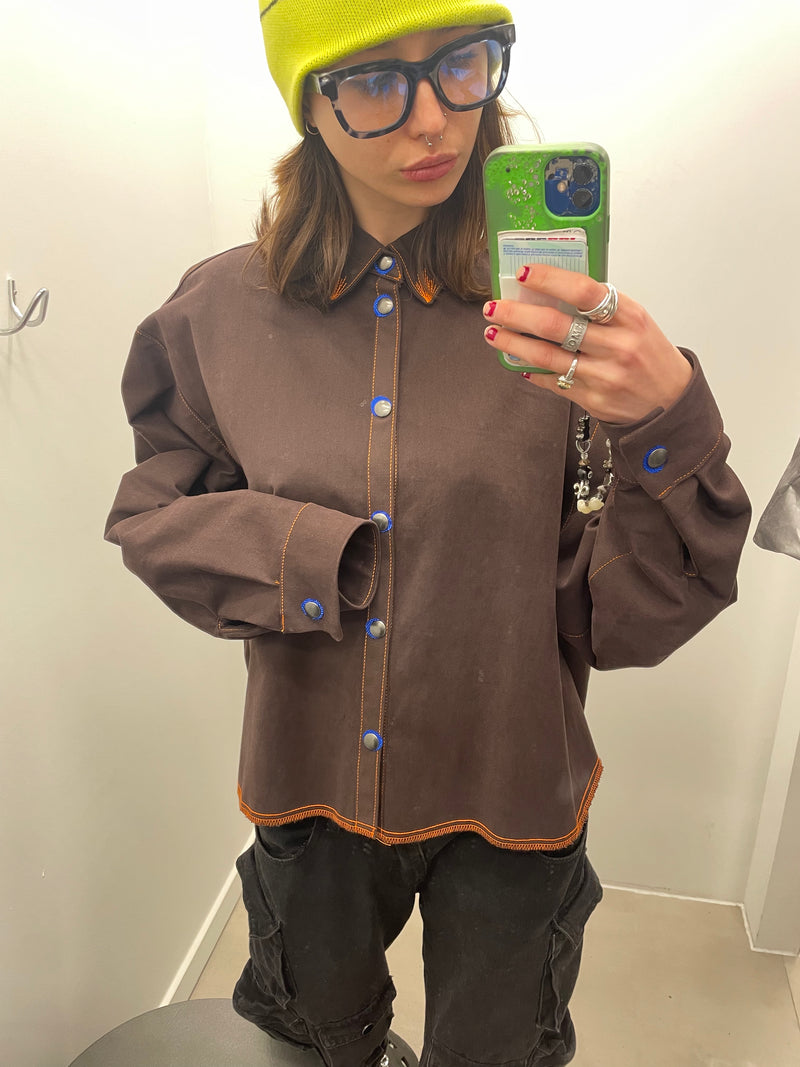 Person wearing a brown jacket with blue buttons, black pants, and a green beanie taking a mirror selfie.