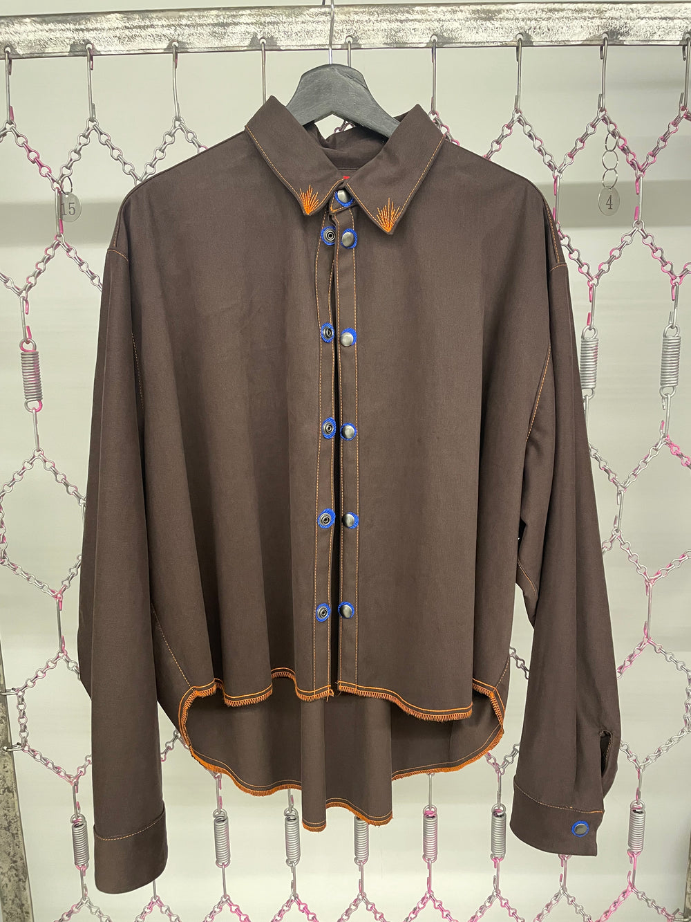 Brown shirt with blue buttons on a hanger against a patterned wall.