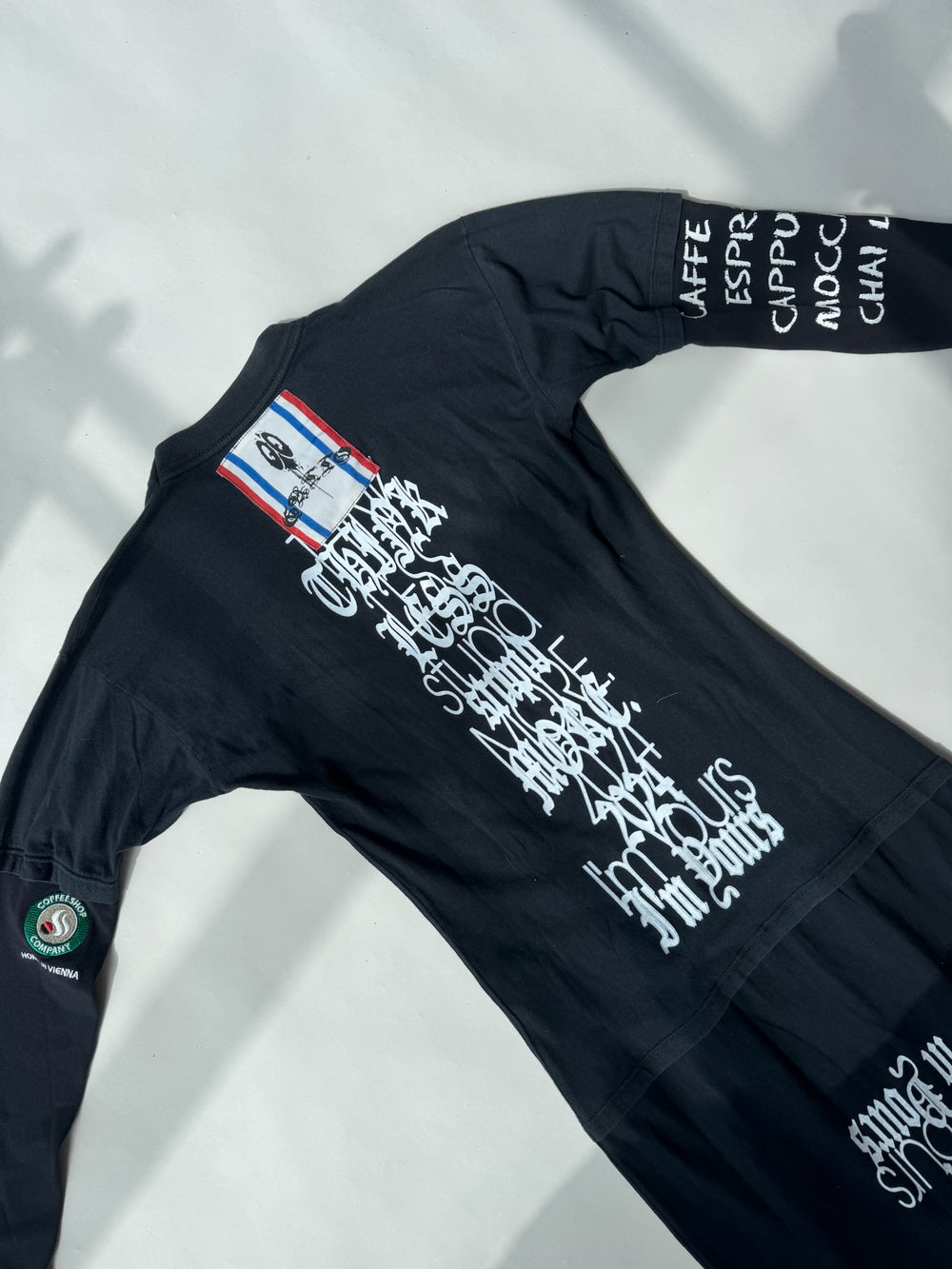 Back detail of GATTO des F*CKDOWN black maxi dress featuring white gothic typography reading ‘Think Less, Studio Simple Mode’ with ‘2024 I’m Yours’ at the bottom, and a red-white-blue patch with skateboard graphic near the colla