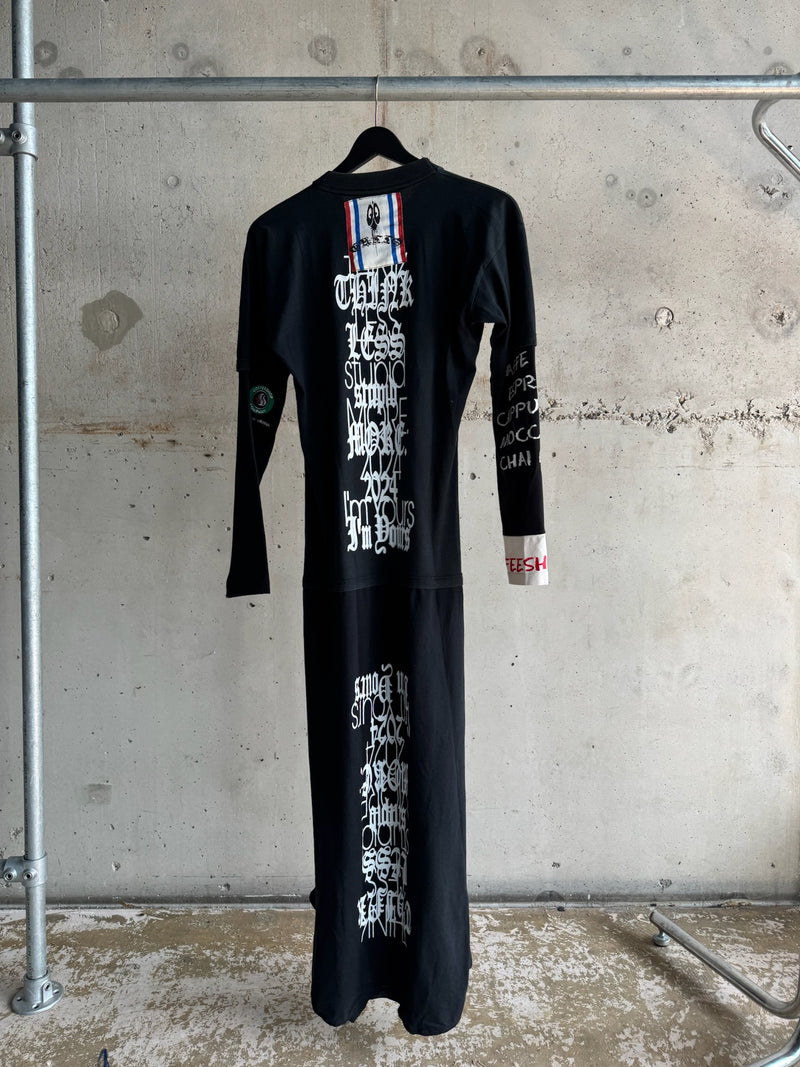 Back view of black graphic maxi dress featuring gothic white text reading ‘Think Less Stupid More Sex 2024 I’m Yours’, hand-painted sleeve details, and stitched ribbon patch at the neckline