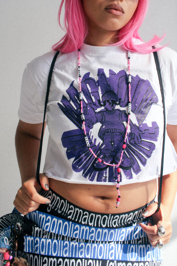 Model wearing a Magnolia cropped graphic T-shirt with purple print, styled with layered Magnolia logo straps worn as belts and accessories.
