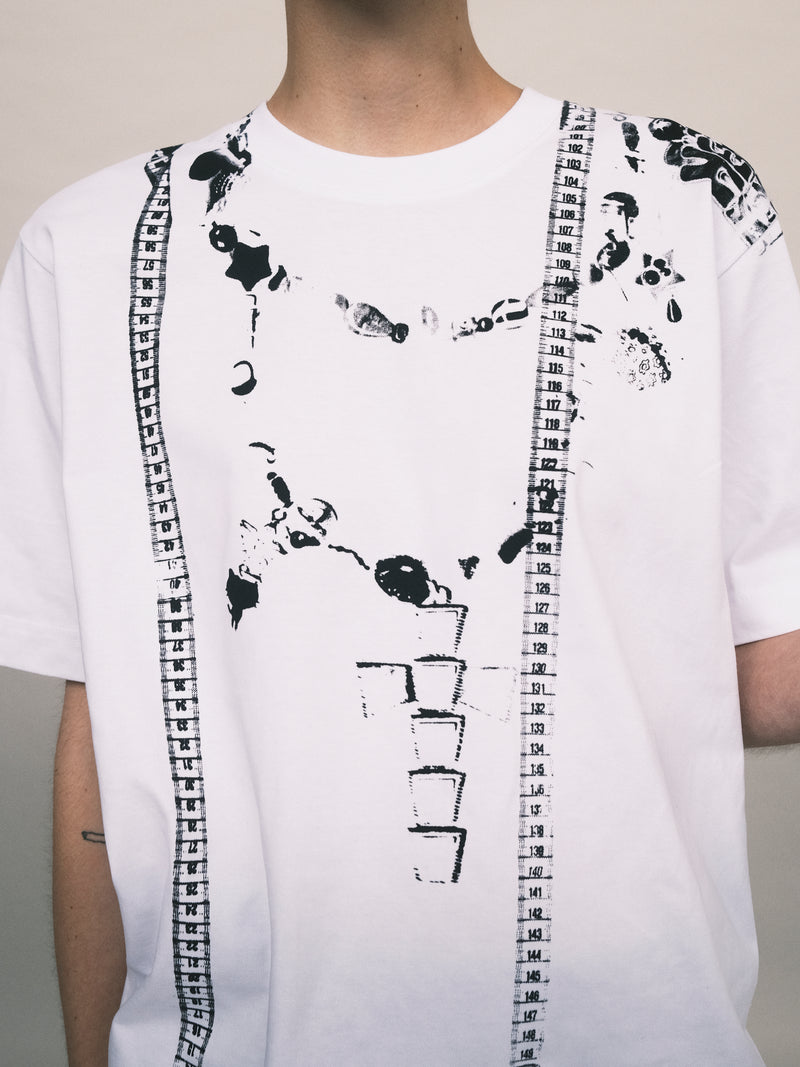 White T-shirt with abstract black graphics, including a measuring tape design running vertically along one side and splatter-like prints scattered across the chest. The unconventional pattern adds a unique, edgy touch to the garment, blending minimalist style with artistic detail.