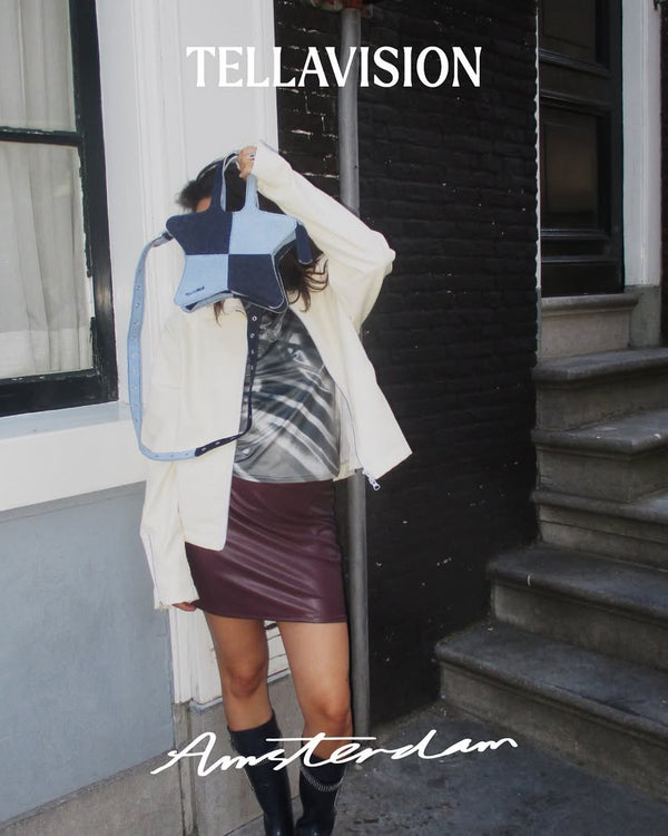 Model holding blue Tellavision patchwork star bag on Amsterdam street wearing layered styling and knee high boots