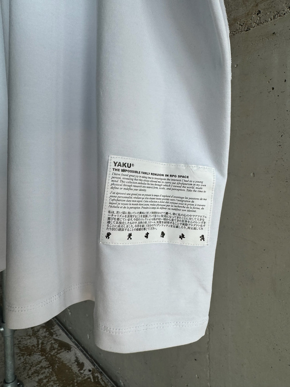 Close-up of YAKU® white T-shirt featuring multilingual Afrofuturism-inspired patch titled ‘The Impossible Family Reunion in RPG Space
